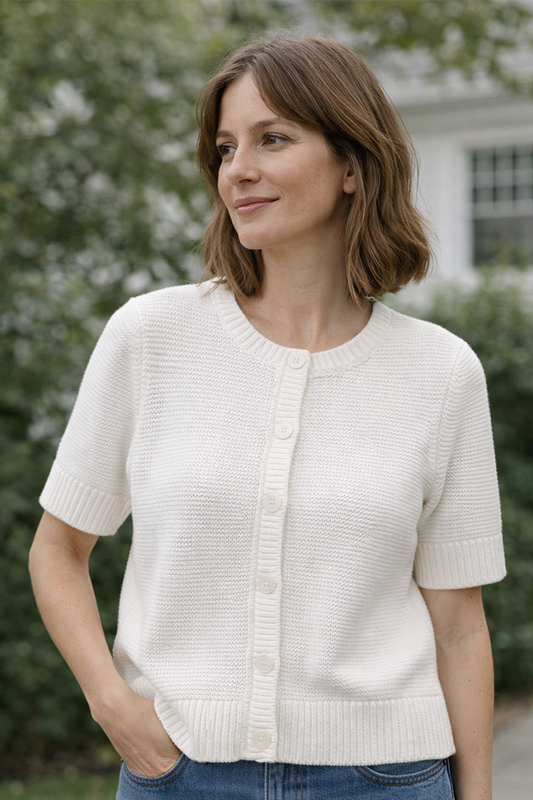 Woman wearing a white knit cardigan outdoors with greenery in the background
