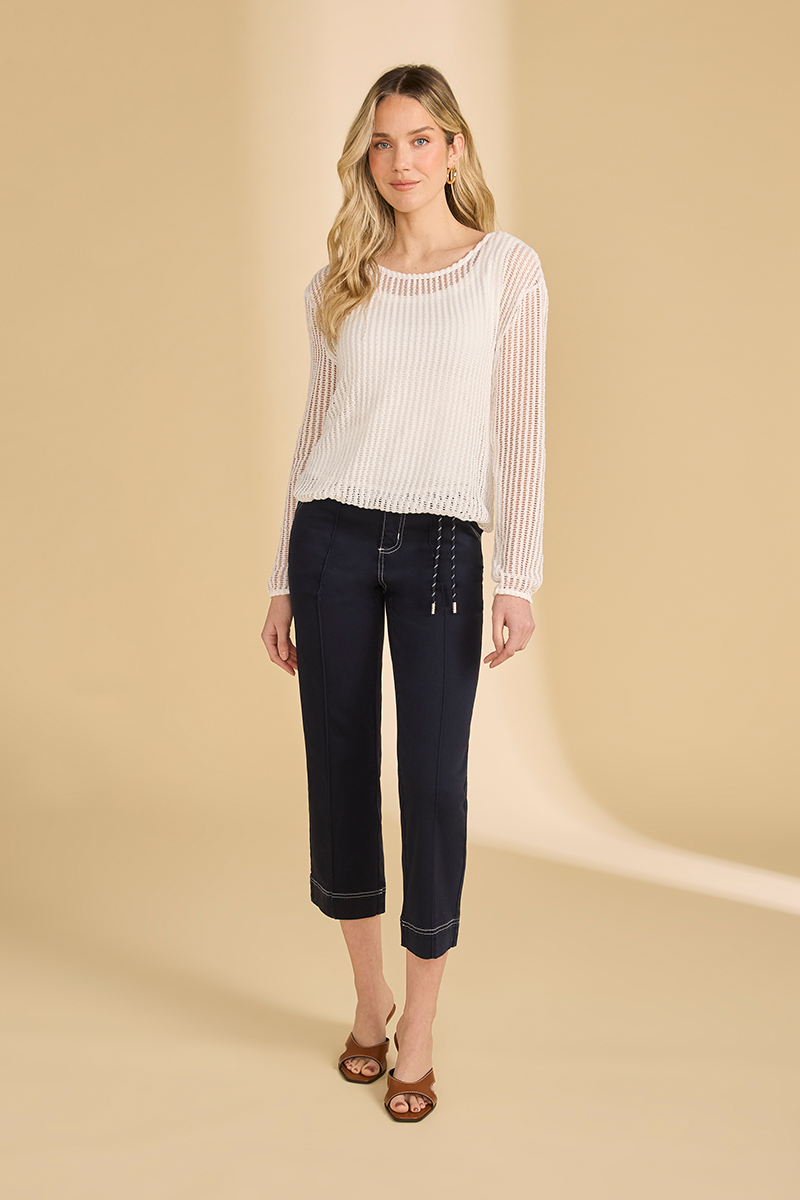 Woman wearing a white open knit sweater
 and dark jeans on a beige background