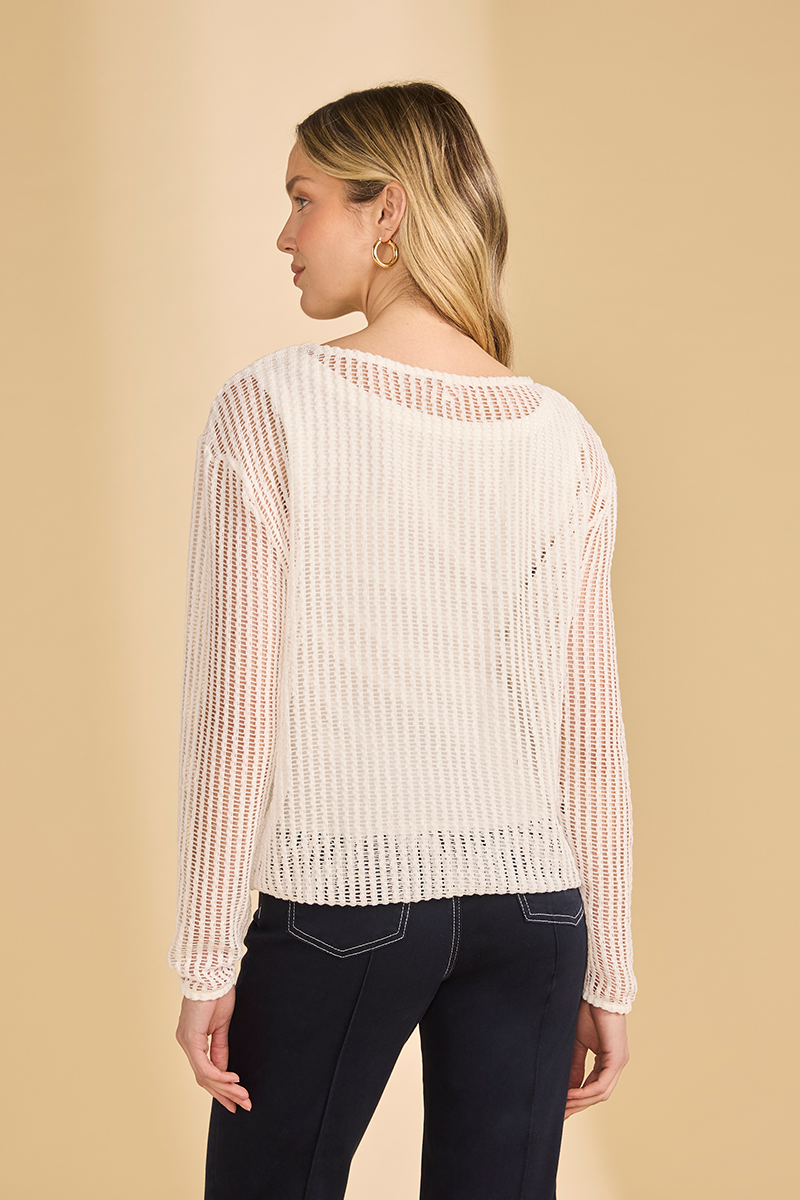 Woman wearing a white open knit sweater and dark jeans on a beige background