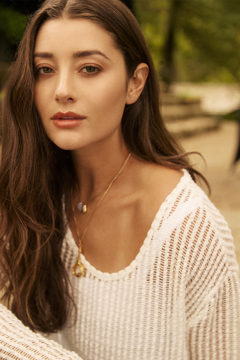 Woman wearing a white knit sweater with a blurred outdoor background