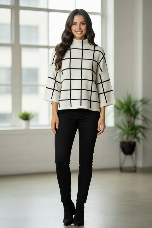 Woman wearing a black and white checkered sweater and black pants in a bright room with large windows.