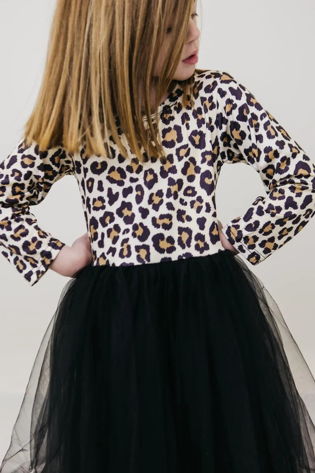 A child wearing a long-sleeve leopard-print top with a black tulle skirt, shown from the side against a plain light background.