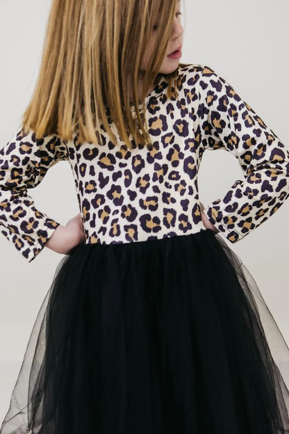 A child wearing a long-sleeve leopard-print top with a black tulle skirt, shown from the side against a plain light background.